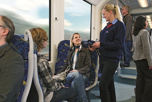 Fahrzeugbegleiterin in Uniform unterhält sich mit zwei Reisenden im Nahverkehrszug